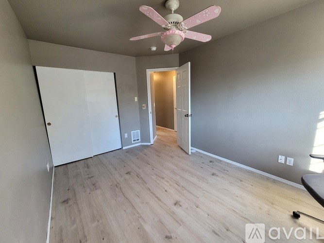 A room with a pink fan and wooden flooring.