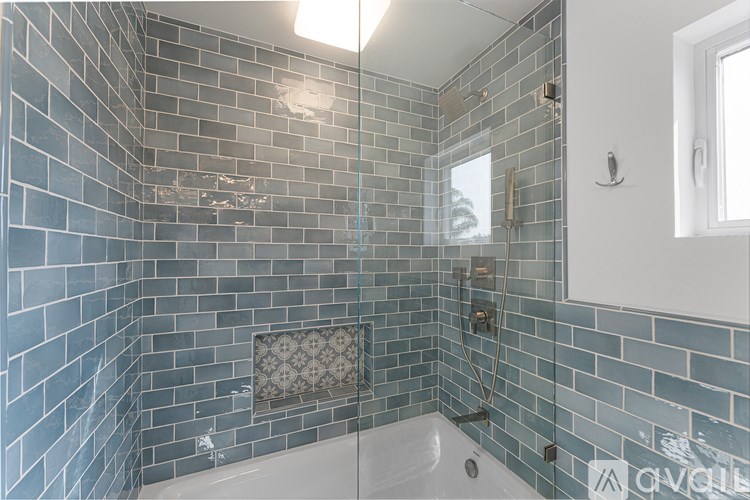 A bathroom with a blue tiled shower and a white tub.