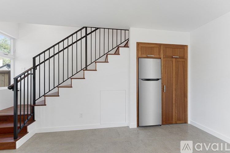 A staircase with a metal railing and wooden steps leads to an empty room with a white wall and a wooden door.