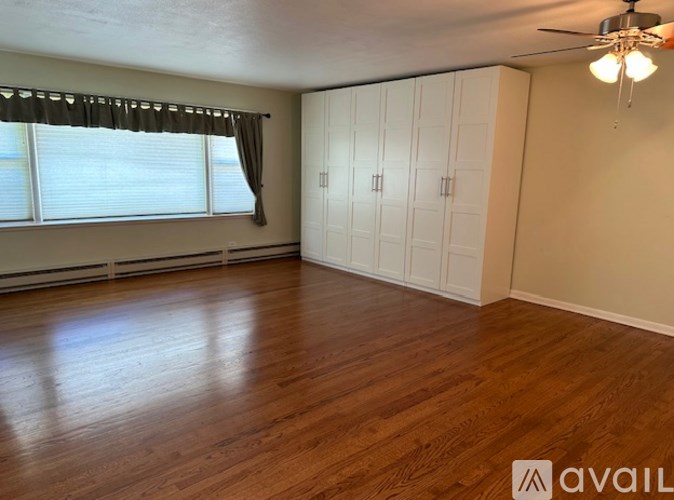 A room with wooden floors and white walls, featuring a window with blinds and a ceiling fan.
