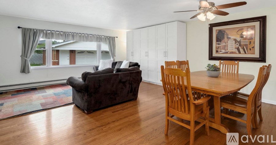 A living room with a brown couch, wooden chairs, and a ceiling fan.