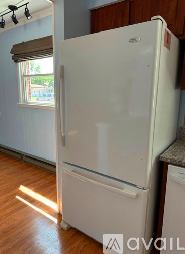 A white refrigerator in a kitchen with wooden floors and a window with blinds.