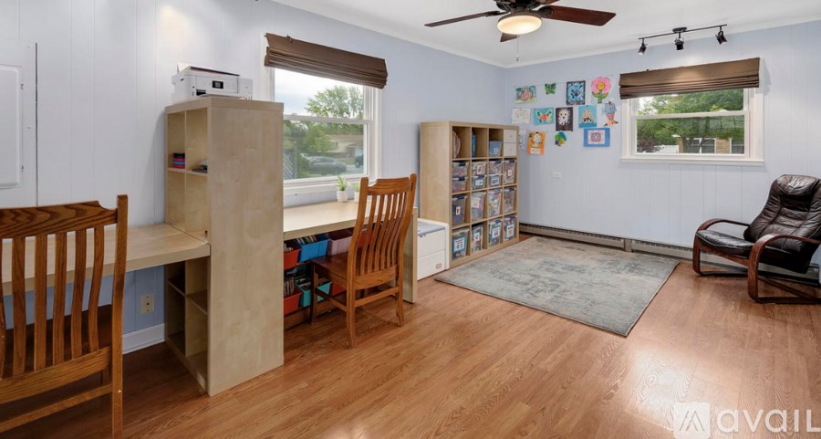 A room with wooden floors and furniture, a ceiling fan, and a window with blinds.