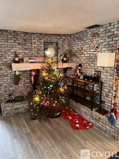 A Christmas tree is decorated with lights and ornaments in a living room with a fireplace.