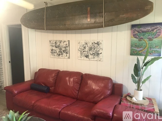 A red leather couch with a surfboard hanging above it.