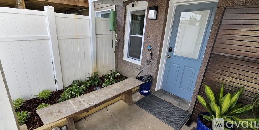 A small backyard with a wooden bench, a white fence, and a blue door.