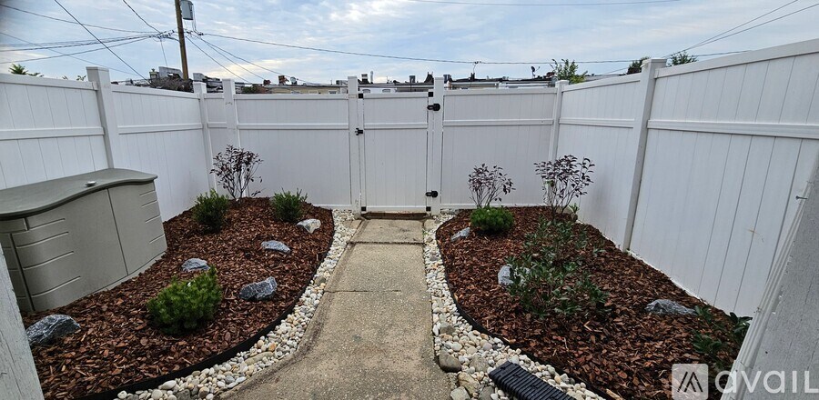A backyard with a white fence and a garden bed with red mulch.