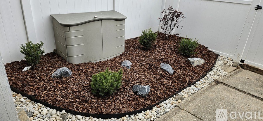 A garden with a grey planter and a white fence.