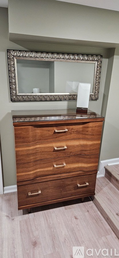 A wooden chest of drawers with a mirror above it.