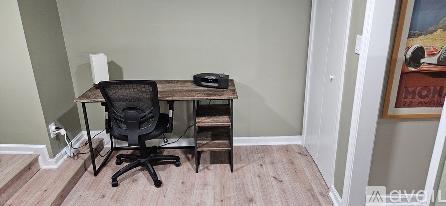 A black chair is in front of a desk with a laptop and a printer on it.