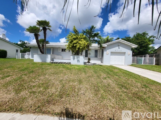 A white house with a driveway and a tree in front.