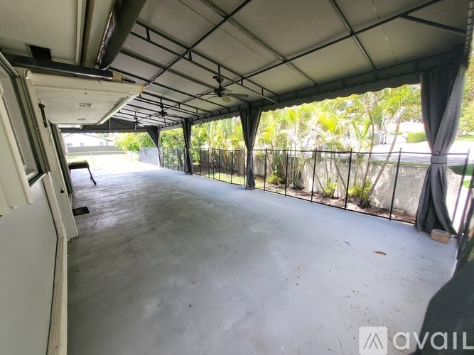 The image shows an empty covered parking area with a concrete floor and a metal fence on one side.