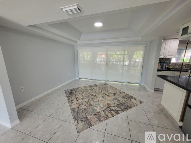 A spacious room with a marble floor mat and a kitchen area to the right.