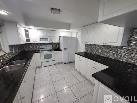 A kitchen with white cabinets and black countertops.
