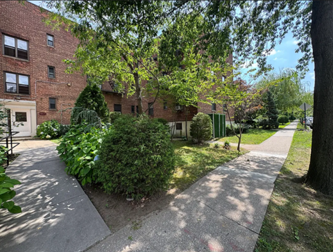 A tree-lined walkway leads to a brick building.
