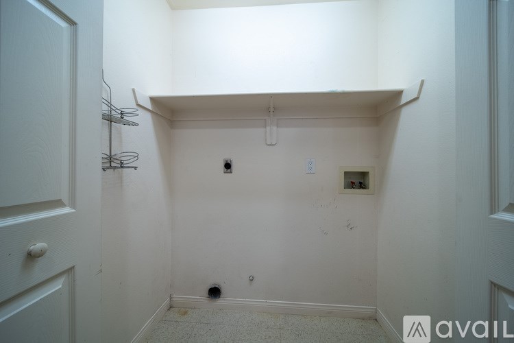 A white hallway with a door on the left and a wall-mounted shelf on the right.