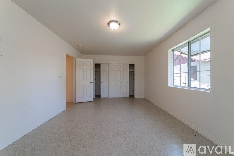 A spacious room with a window, carpeted floor, and two doors.