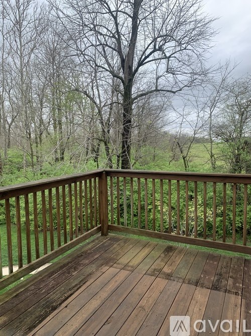 A wooden deck overlooks a grassy field and trees.