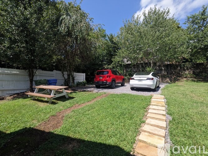 A backyard with a picnic table, a red truck, and a white car.