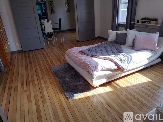 A bedroom with a bed, wooden floor, and a rug.