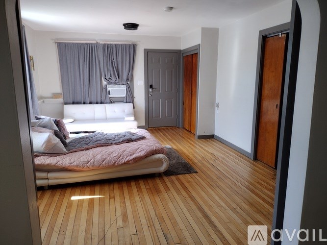 A bedroom with a bed, a window with curtains, and a wooden floor.