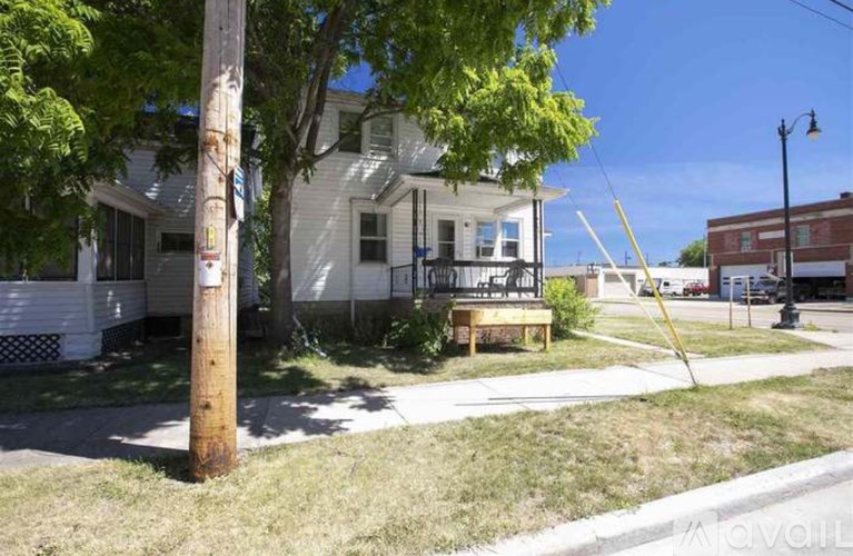 A white house with a porch and a tree in front.