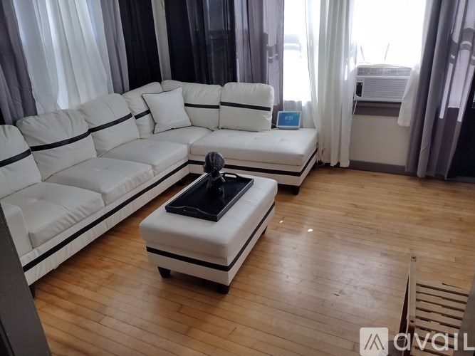 A white sofa with a black cushion is in the middle of a room with wooden flooring and curtains.