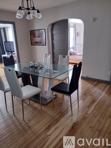 A glass dining table with four chairs in a room with wooden flooring.