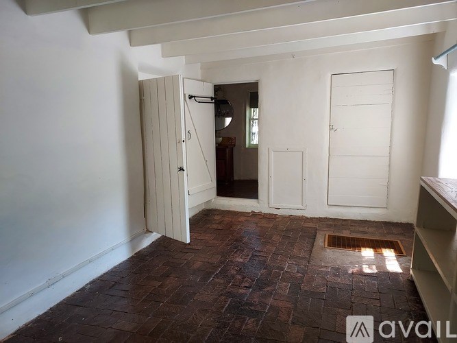 A room with a brown floor and white walls has a door open to a hallway.