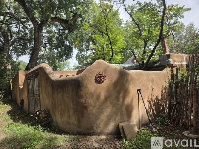 A small mud hut with a door and a window is surrounded by trees.