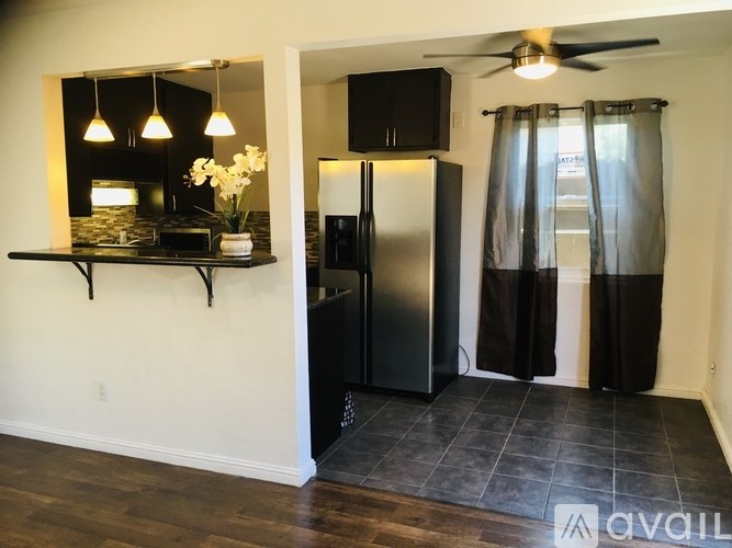 A kitchen area with a refrigerator, a fan, and a dining table with a vase of flowers.