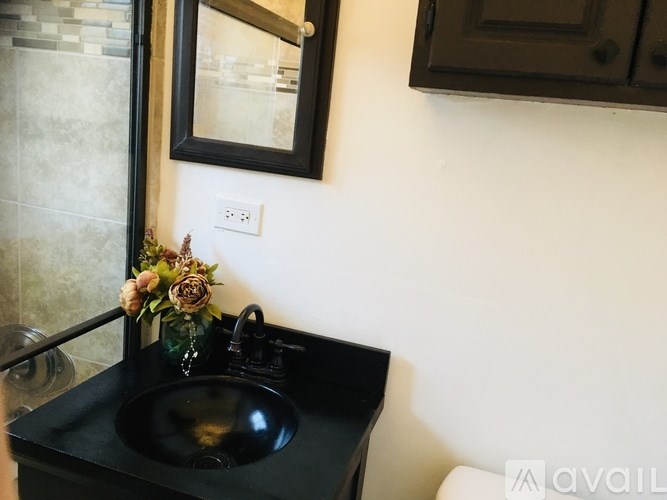 A black sink is in a black vanity with a flower arrangement on the counter.
