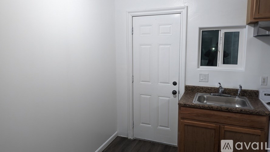 A white door is in a small kitchen with a sink and a window.