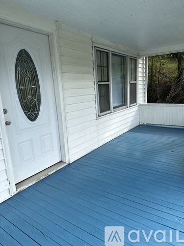 A white door with a glass window is on the left side of a porch with blue wooden planks.