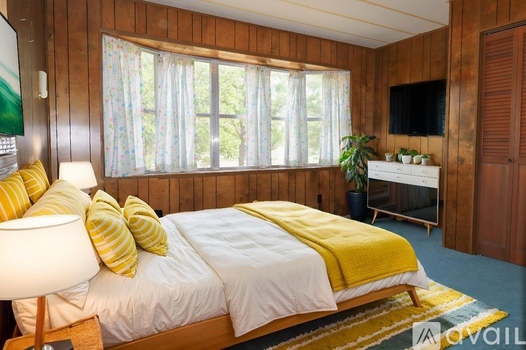 A bedroom with a bed, a lamp, a TV, and a window with curtains.