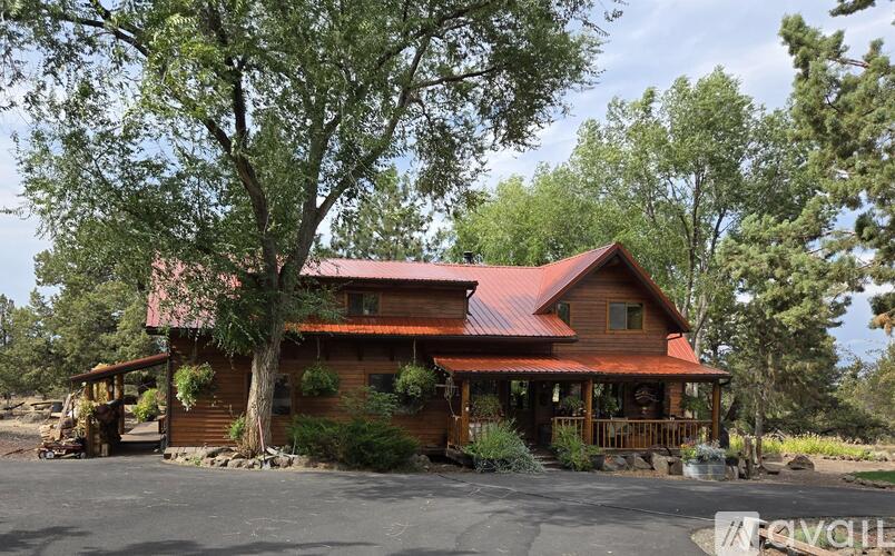 A house with a red roof and a porch surrounded by trees.