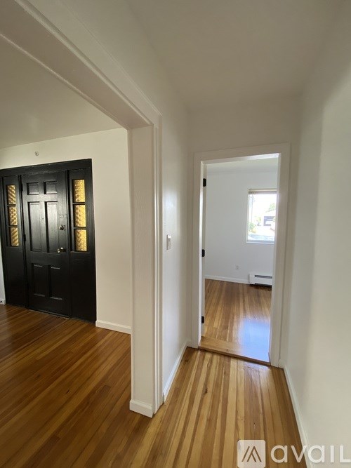 A hallway with a black door and wooden floors.
