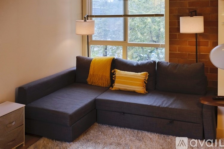 A grey couch with a yellow throw pillow sits in front of a window.