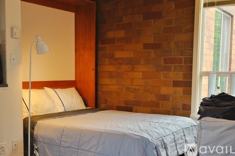 A bed with a white comforter is in a room with a brick wall.