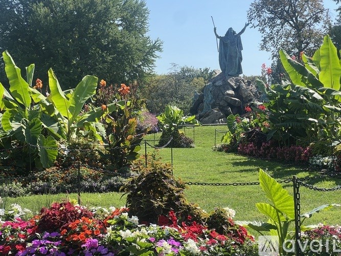 A garden with a variety of flowers and a statue in the background.