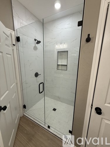 A bathroom with a glass shower door and a white door.