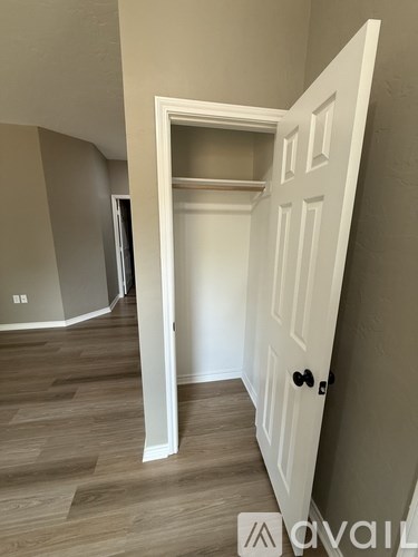 A white door is open to a hallway with wood flooring.