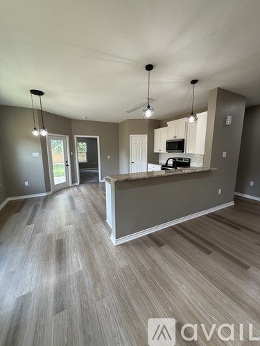 A spacious kitchen and living room with wood flooring and pendant lights.