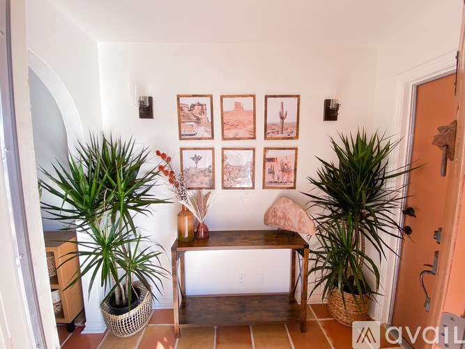 A hallway with a bench, potted plants, and pictures on the wall.