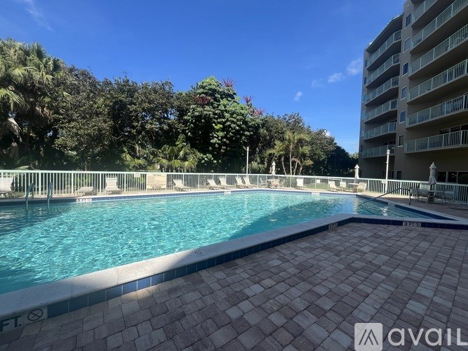 A large outdoor swimming pool surrounded by a tiled floor and a white fence.