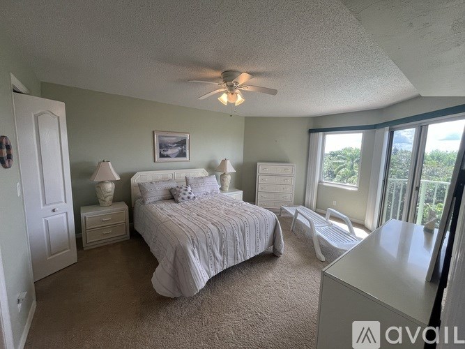 A bedroom with a large bed, a ceiling fan, and a view of the outdoors through a sliding glass door.