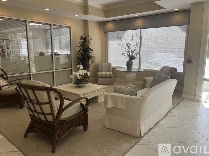 A living room with a white couch, a wooden chair, and a glass table with a vase of flowers on it.
