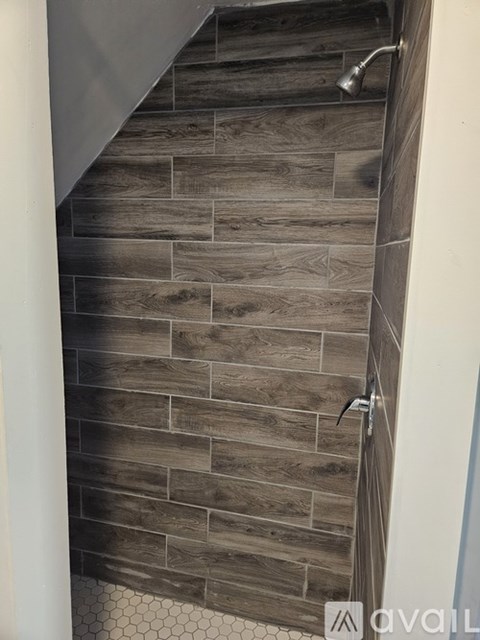 A bathroom with a tiled wall and a shower head.