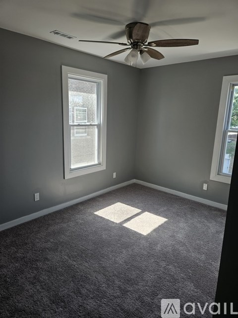 A room with a ceiling fan and two windows.