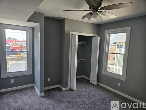 A room with a ceiling fan and two windows.